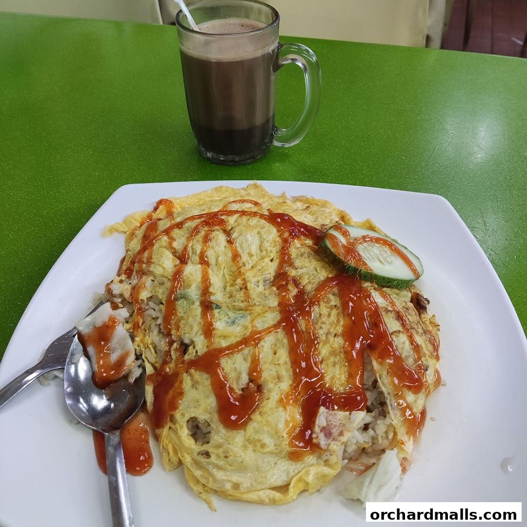 A plate of fried rice topped with omelette and drizzled with chili sauce, served with a drink.