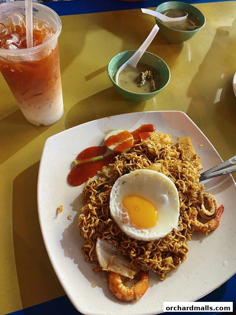 A plate of fried noodles with a fried egg, shrimp, and squid, served with a drink and soup.