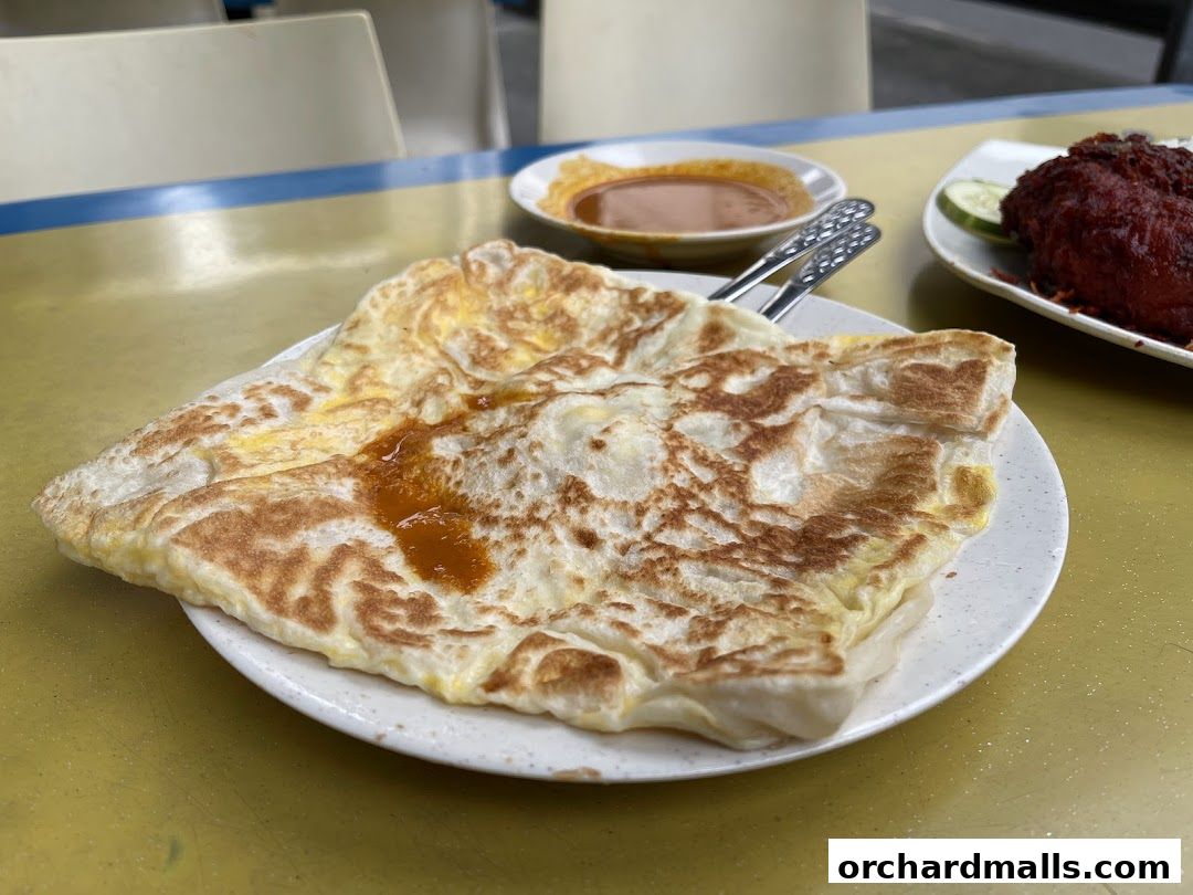 A close-up of a delicious Roti Canai with curry sauce and a side of fried chicken.