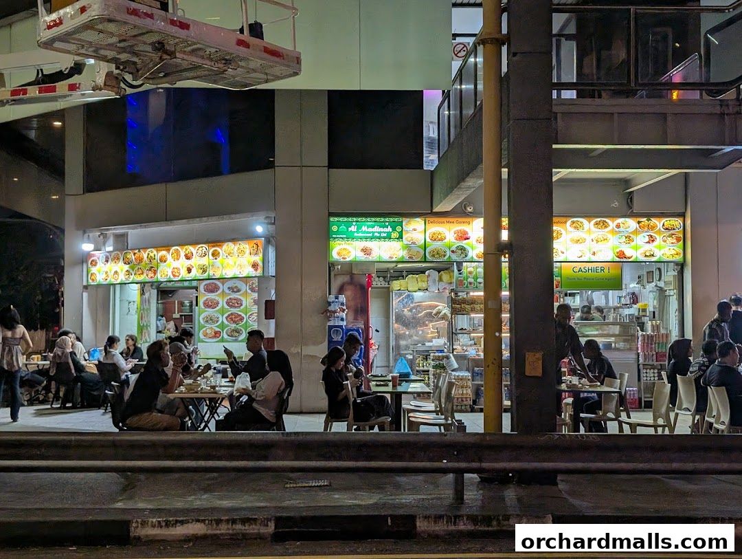Al Madinah Restaurant exterior at night with customers dining and illuminated menu boards.