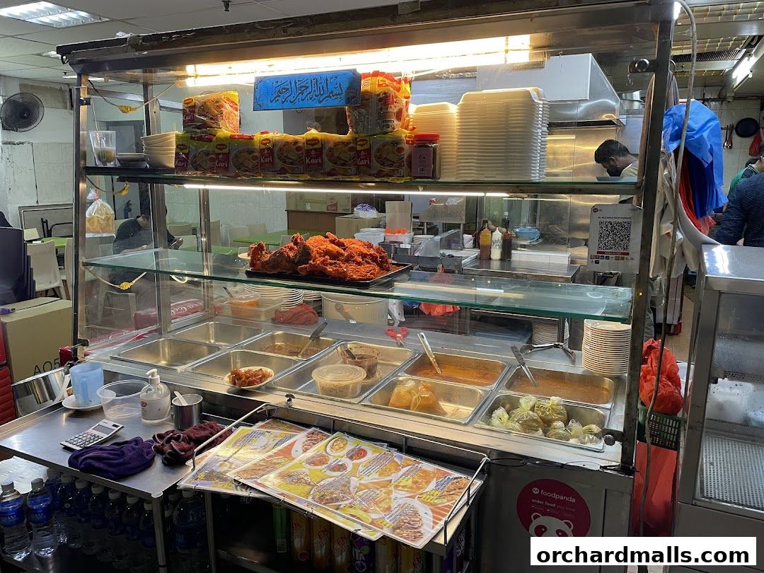 A food stall display with various dishes in metal containers and fried chicken.