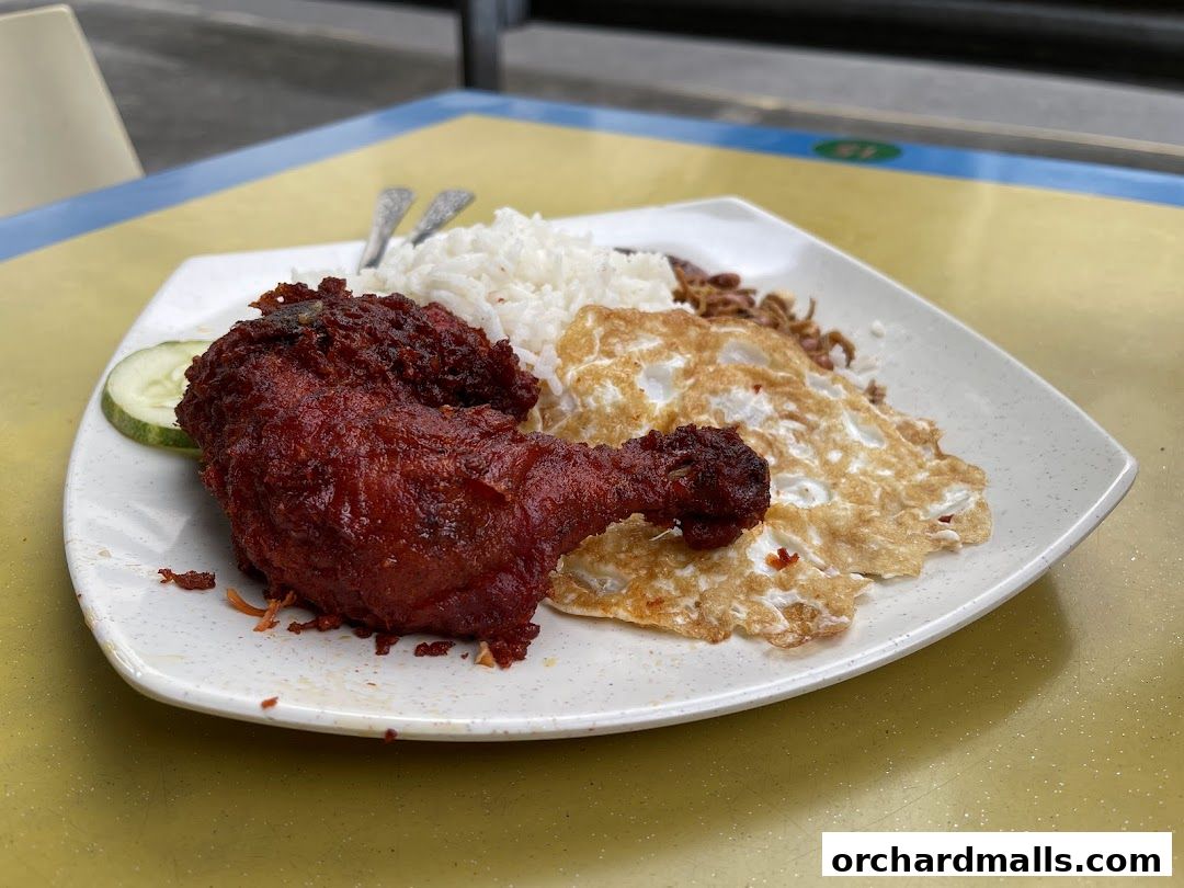 A plate of nasi lemak with fried chicken, fried egg, cucumber, and anchovies.