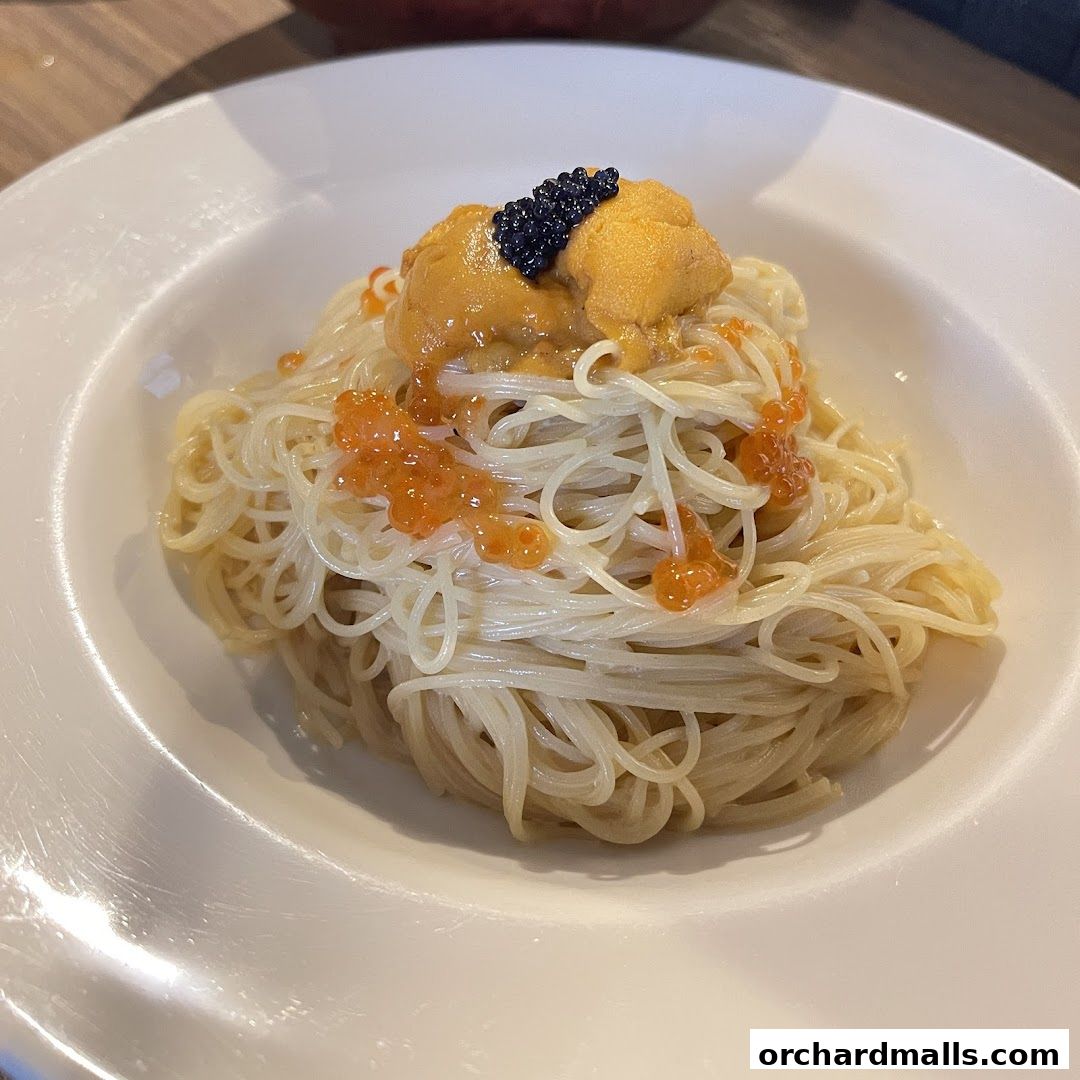 A close-up of pasta topped with uni, ikura, and caviar in a white bowl.