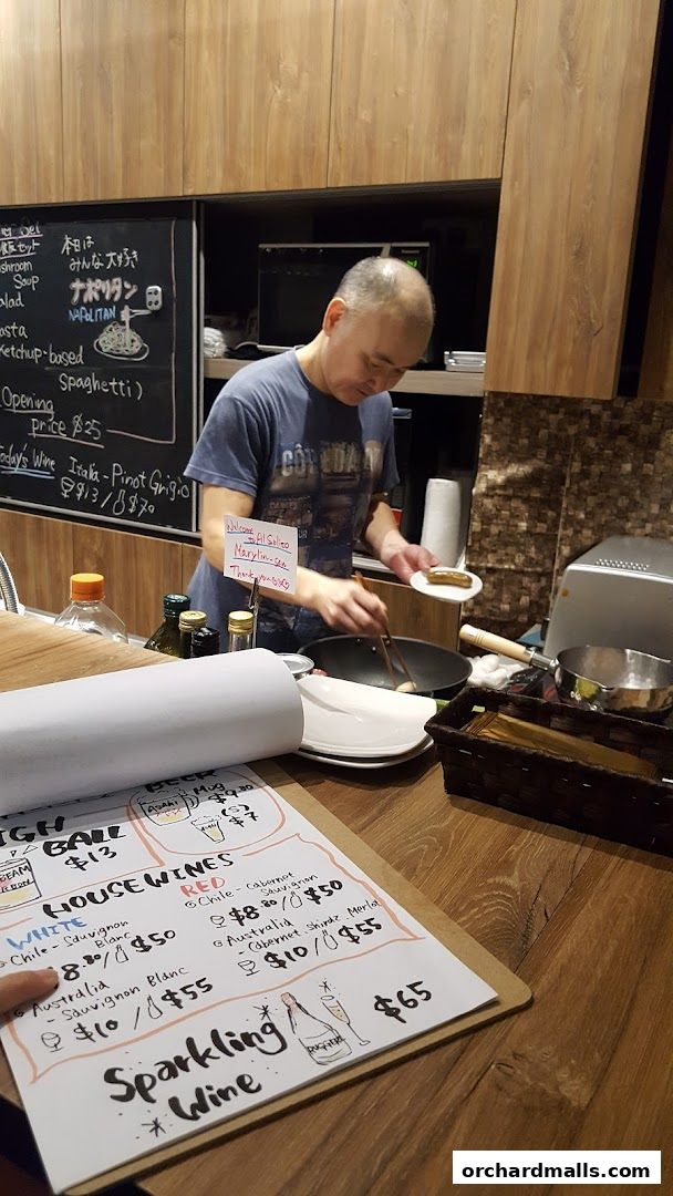 A chef prepares food in a Japanese Italian izakaya with a menu visible.