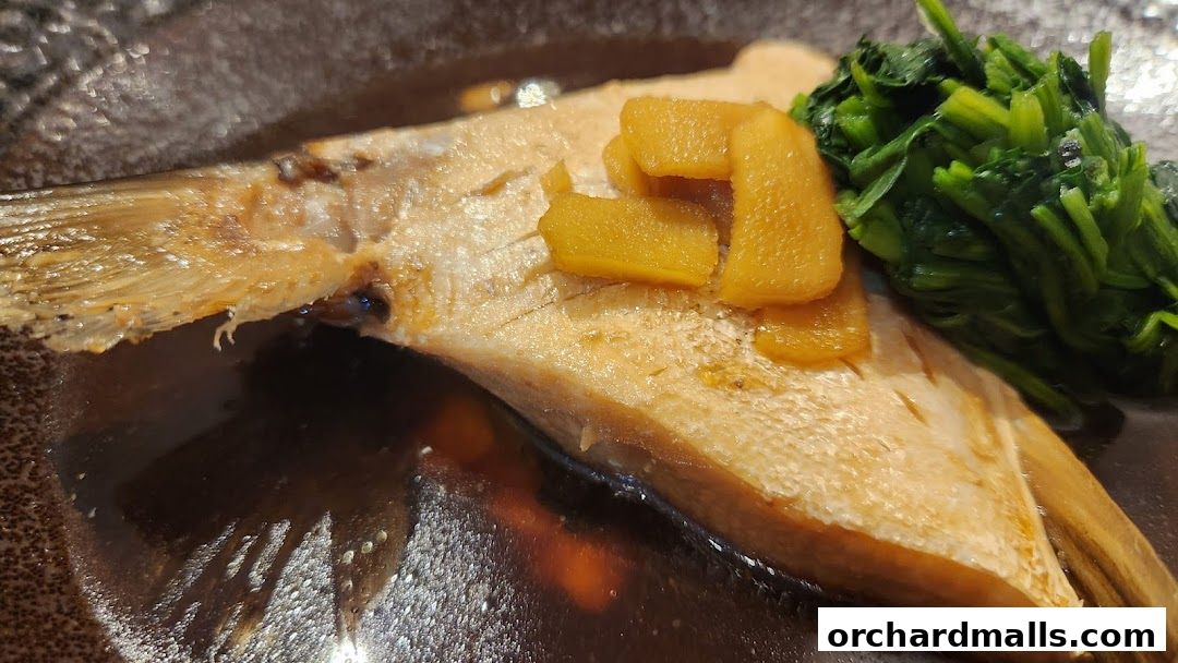 A close-up of a cooked fish dish with greens and ginger on a dark plate.