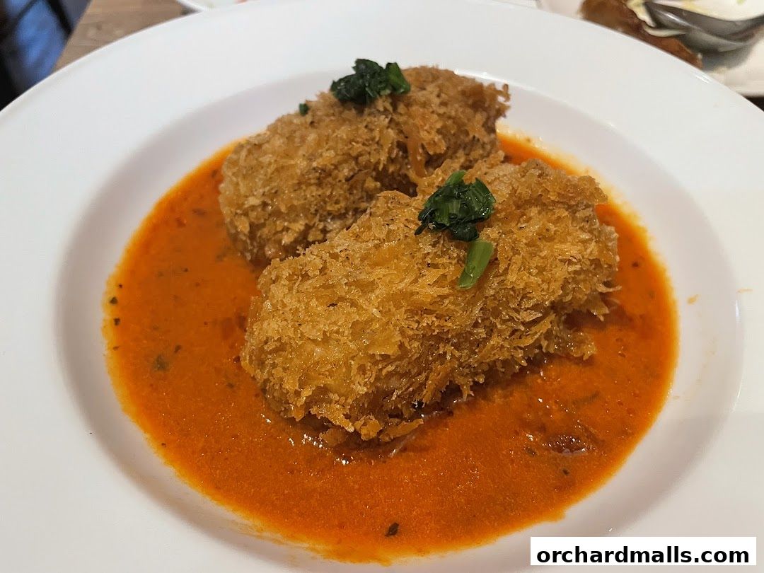 Two breaded cutlets served in a rich, orange sauce with a garnish of greens.