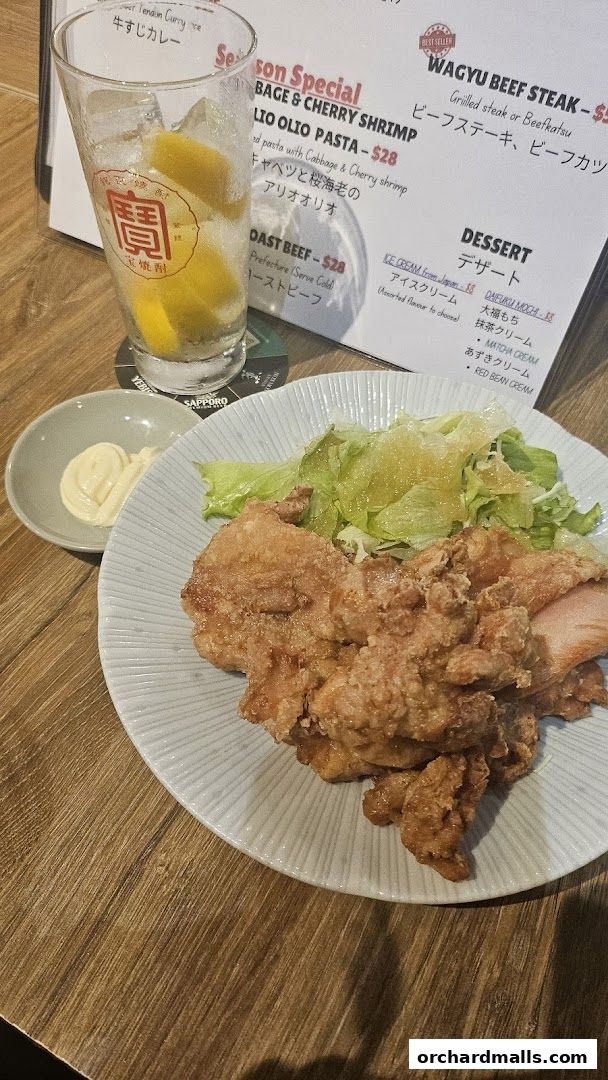 A plate of fried chicken with salad, a glass of drink, and a menu.