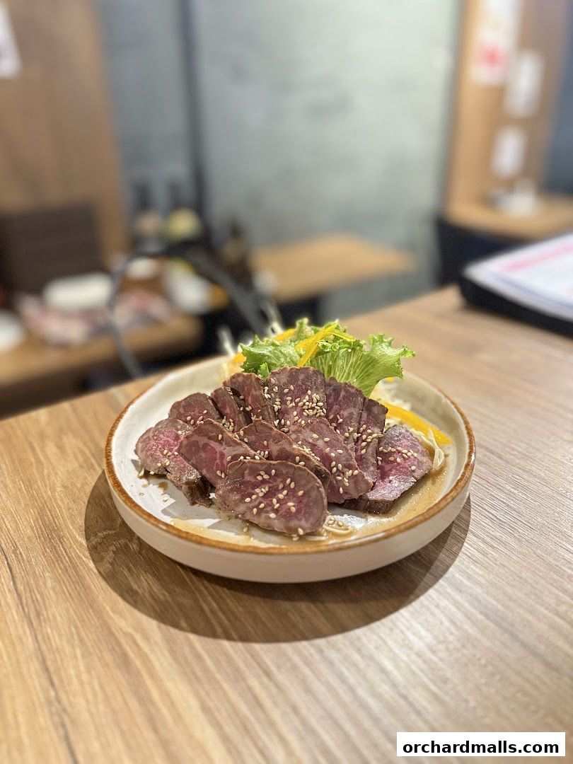 A plate of thinly sliced beef with sesame seeds and a side salad on a wooden table.