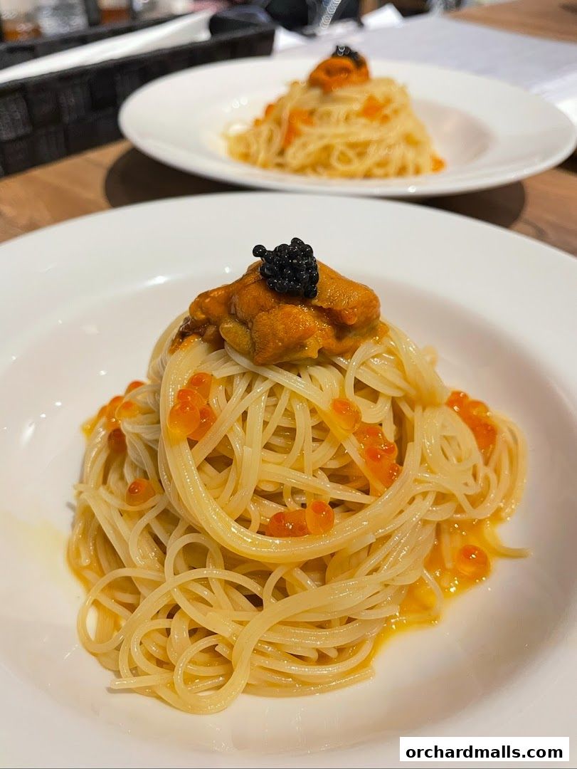 Two plates of spaghetti topped with uni, ikura, and caviar.