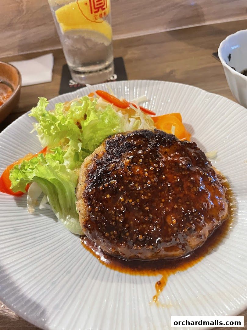 A close-up of a glazed hamburger patty with a side salad and a drink.