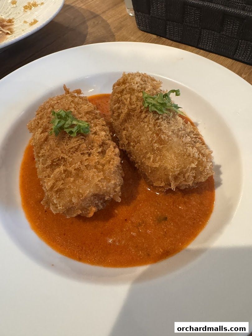 Two crispy fried croquettes served in a rich orange sauce on a white plate.