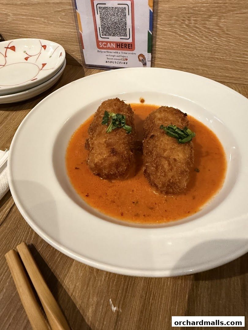 Two breaded croquettes served in a creamy orange sauce with a garnish.