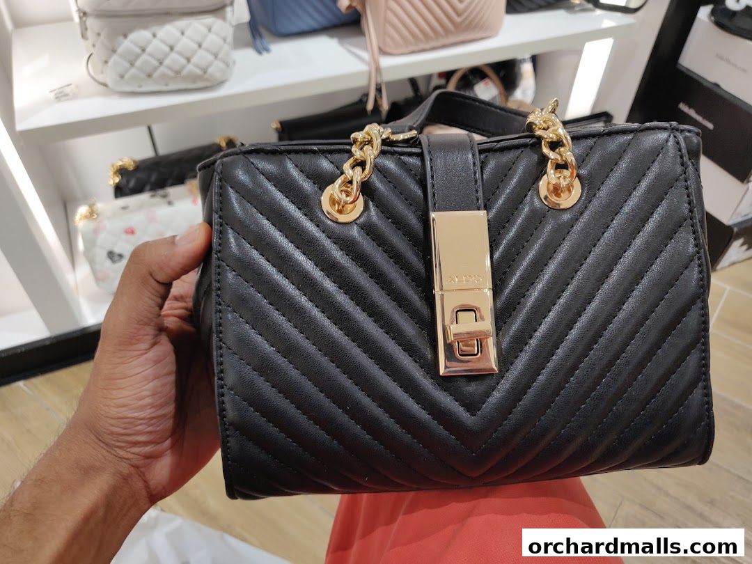 A hand holds a black quilted handbag with gold hardware in a retail store.