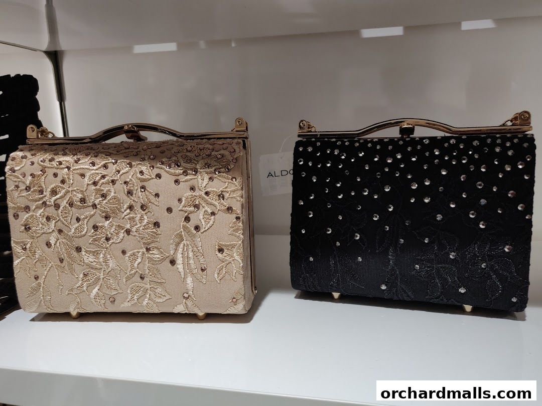 Two embellished clutch bags, one beige and one black, displayed on a white shelf.
