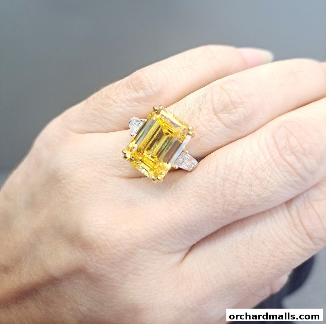 A hand wearing a large, emerald-cut yellow gemstone ring with diamond accents.