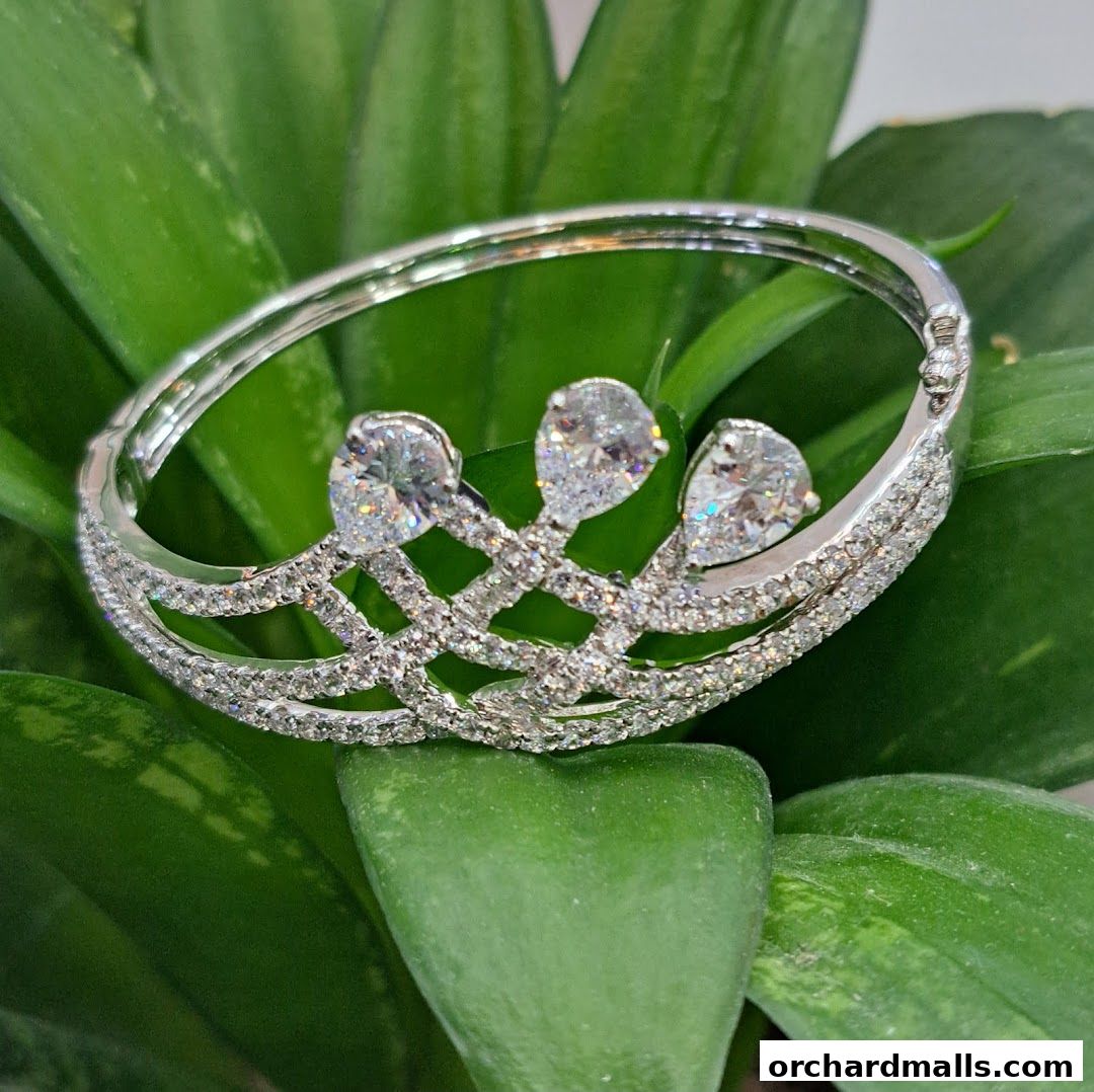 A sparkling silver bracelet with three large diamonds rests on lush green leaves.