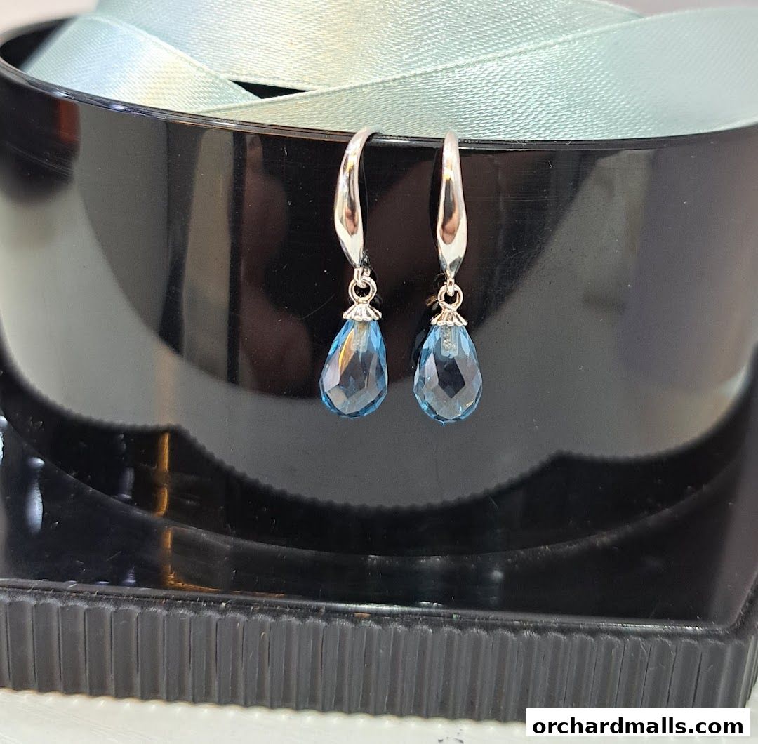 A pair of elegant blue teardrop earrings displayed on a black stand with a light blue ribbon.
