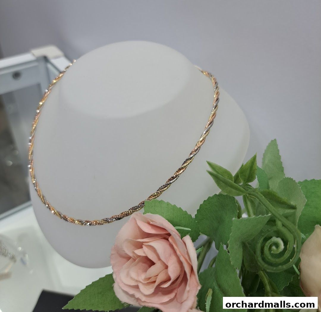 A tri-color twisted necklace displayed on a white bust with pink roses.