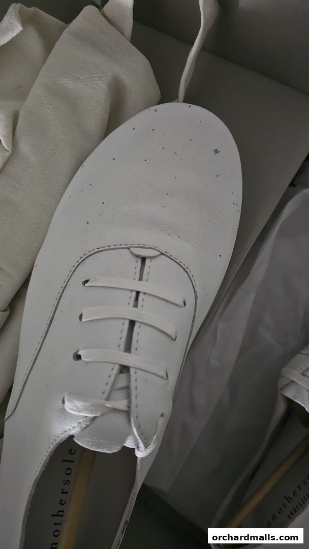 Close-up of a white leather shoe with laces, inside its packaging.