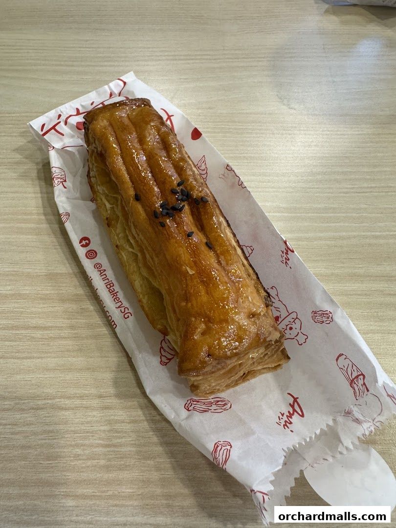 A golden-brown pastry with black sesame seeds on top, wrapped in branded paper.