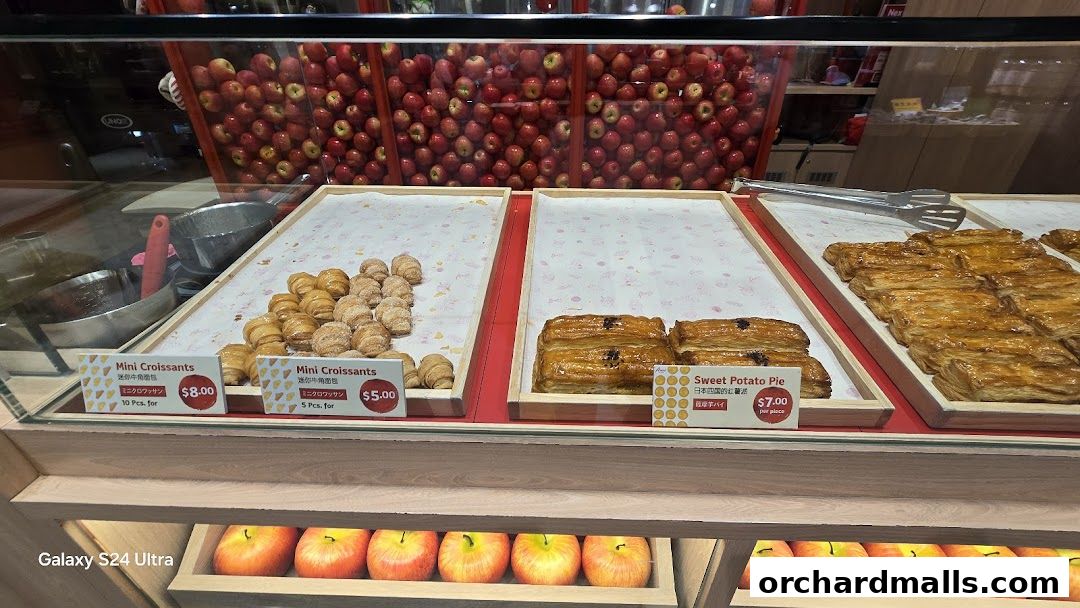 A display case filled with mini croissants and sweet potato pies, with apples in the background.