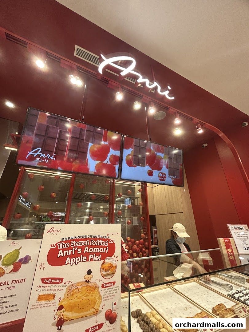 The exterior of Anri Bakery, showcasing its logo, digital displays, and a promotional poster for their apple pie.