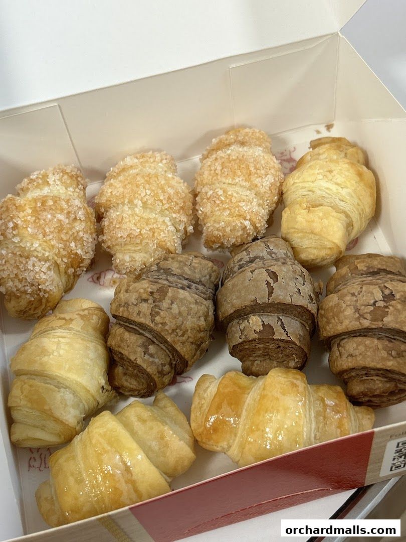 A box filled with assorted mini croissants, some coated in sugar and others plain.