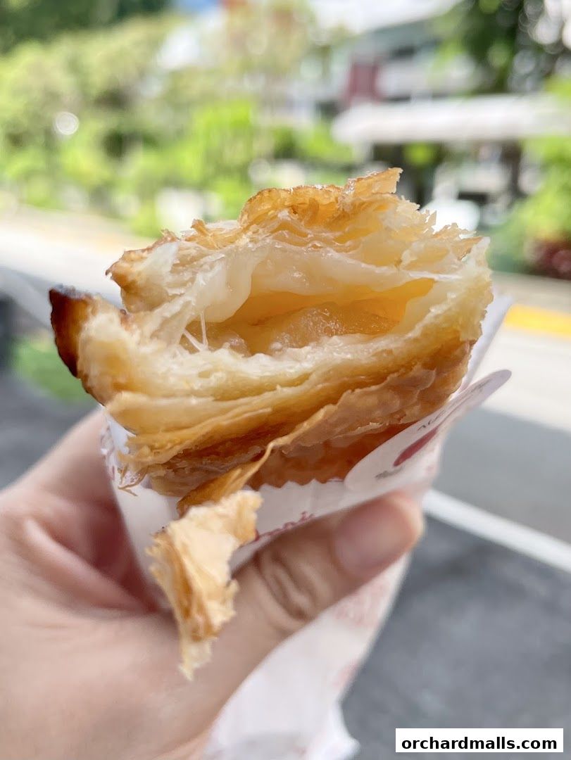 A close-up of a flaky pastry with a creamy filling being held by a hand.
