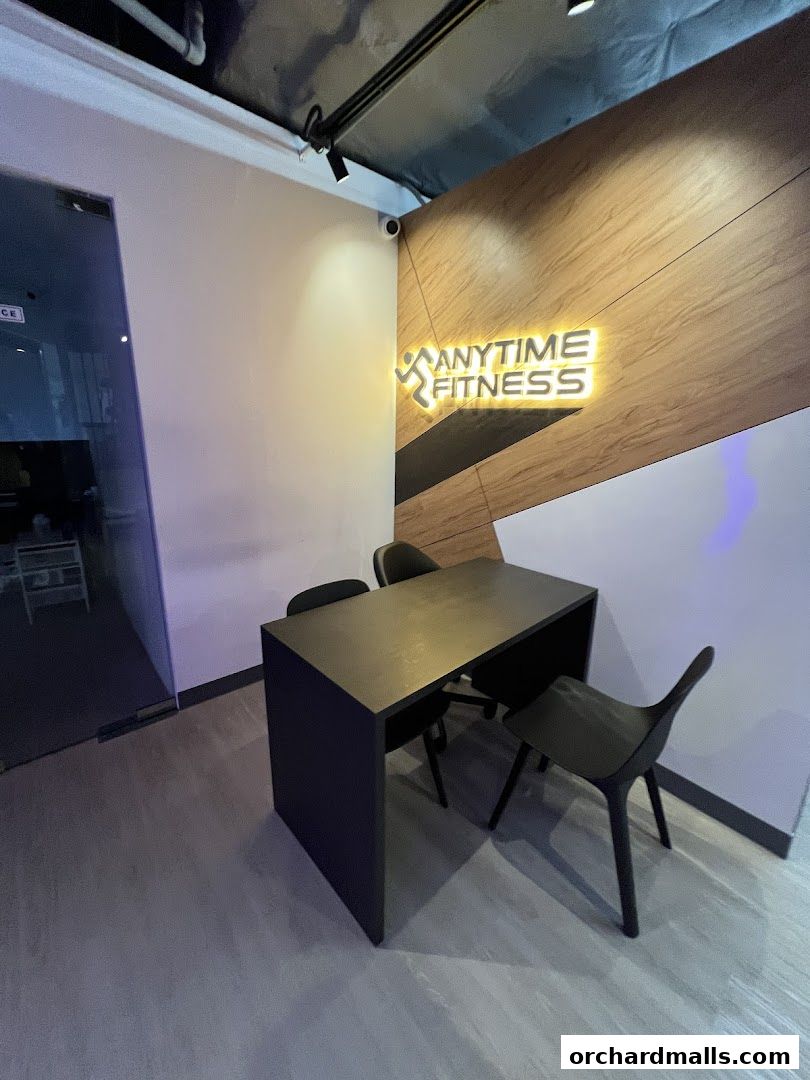 Interior shot of Anytime Fitness Wheelock Place with a desk, chairs, and illuminated logo.