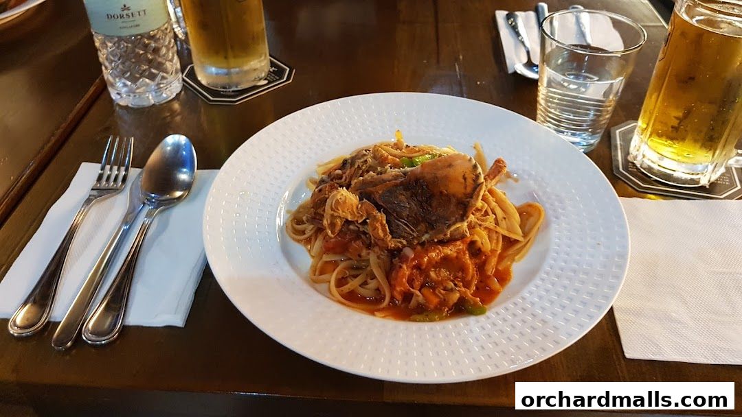 A plate of pasta with soft-shell crab and two glasses of beer on a wooden table.