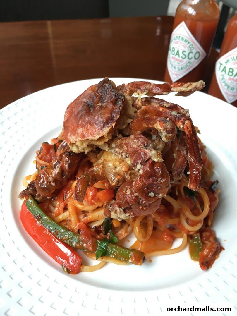 A plate of spaghetti topped with a whole fried soft-shell crab and vegetables.