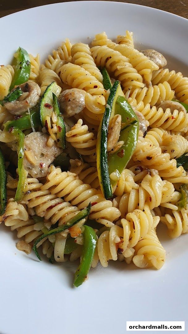 A close-up shot of fusilli pasta with zucchini, bell peppers, and mushrooms in a light sauce.