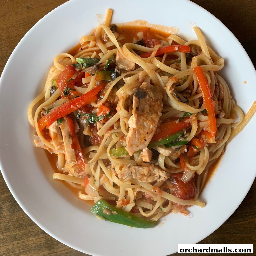 A white plate filled with linguine pasta, chicken, and vegetables in a tomato sauce.