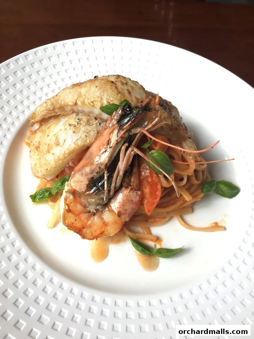 A gourmet dish of grilled fish and shrimp served over pasta with a tomato-based sauce.