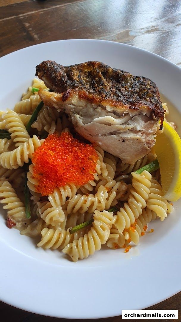 A close-up of a pasta dish with grilled fish, tobiko, and a lemon slice.