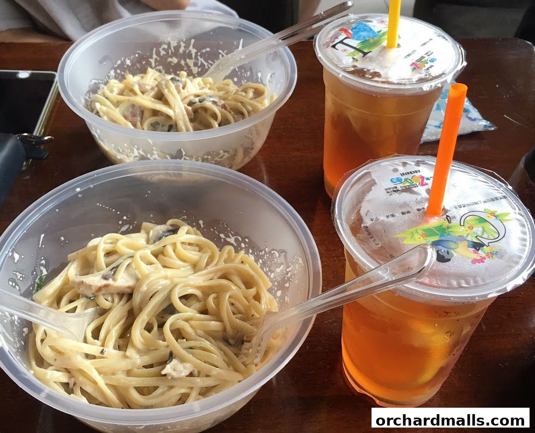 Two bowls of creamy pasta and two iced teas with straws on a wooden table.