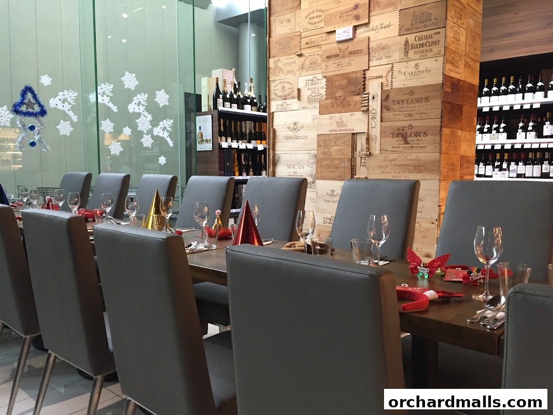 A long dining table set for a festive occasion with wine bottles displayed in the background.
