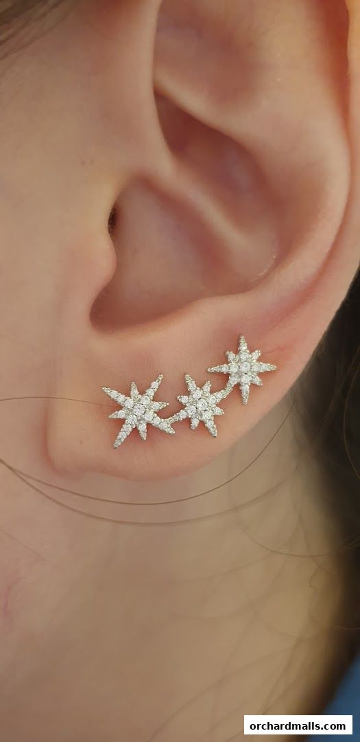 Close-up of a person's ear adorned with sparkling star-shaped ear climbers.