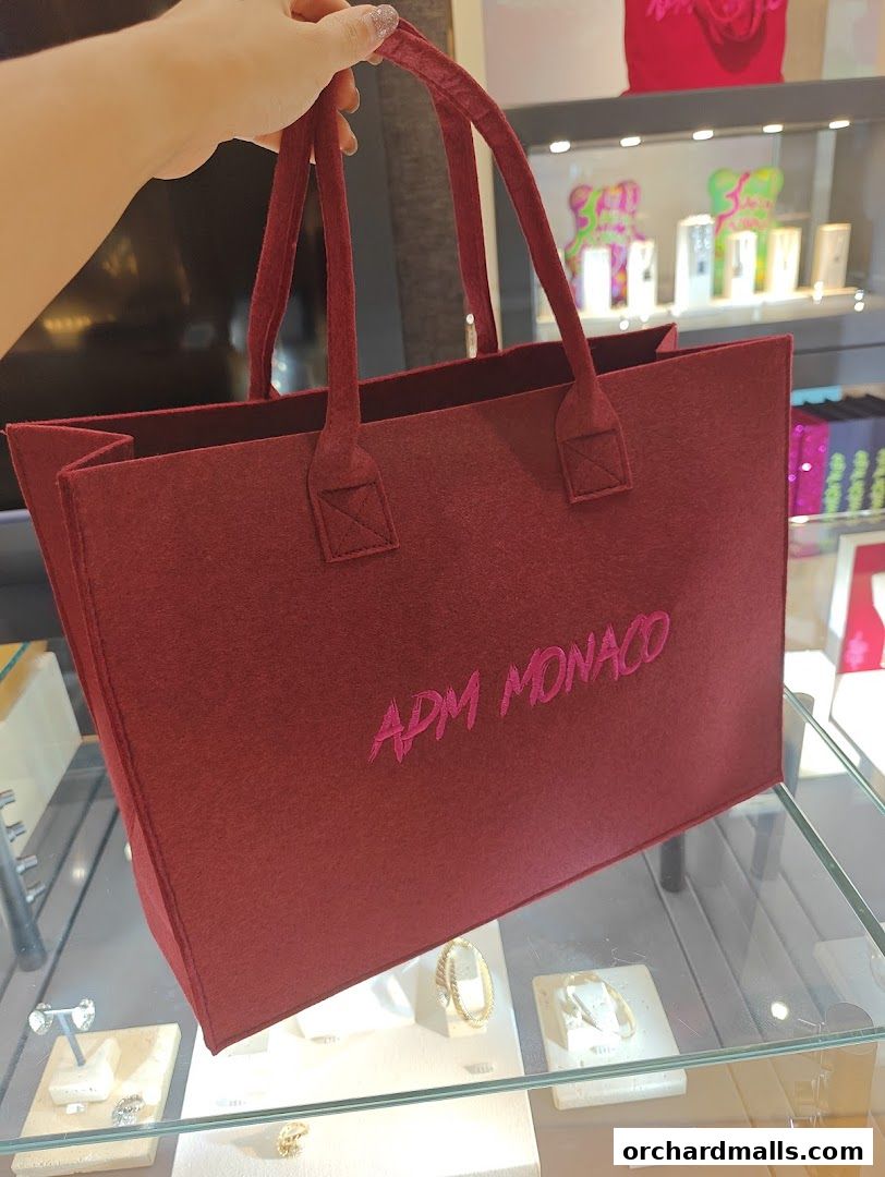 A hand holds a burgundy felt tote bag with APM Monaco logo inside a jewelry store.
