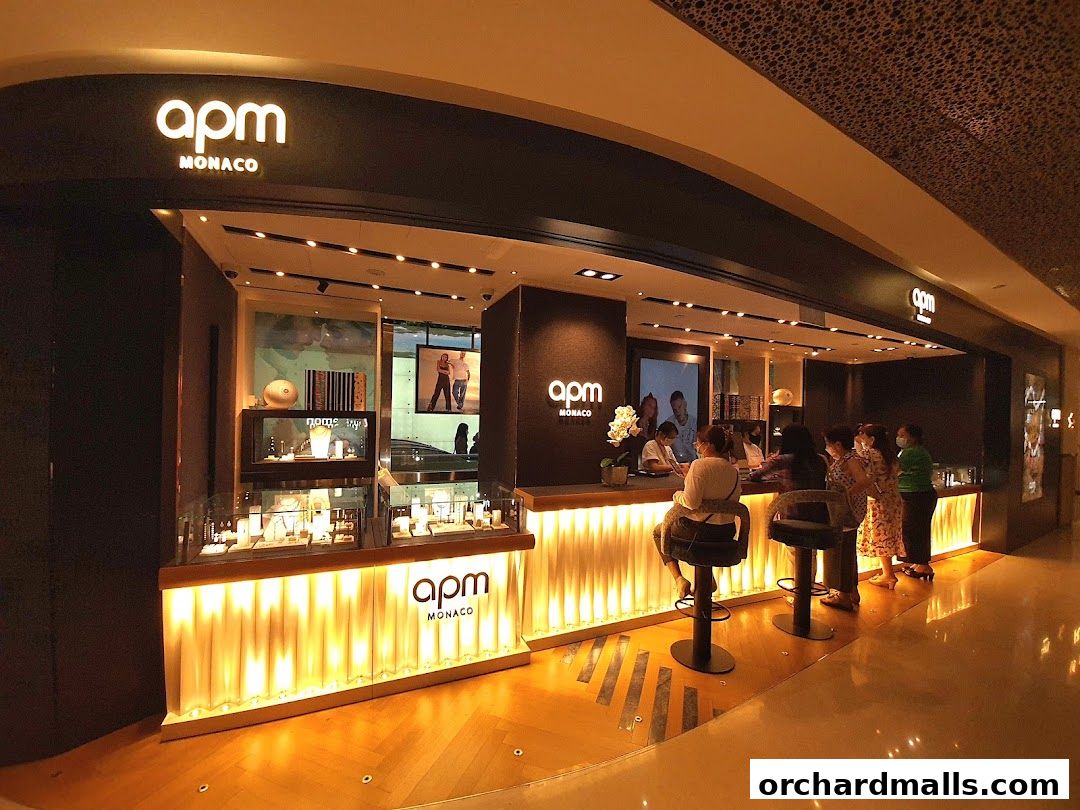 A well-lit APM Monaco jewelry store with customers being served at the counter.