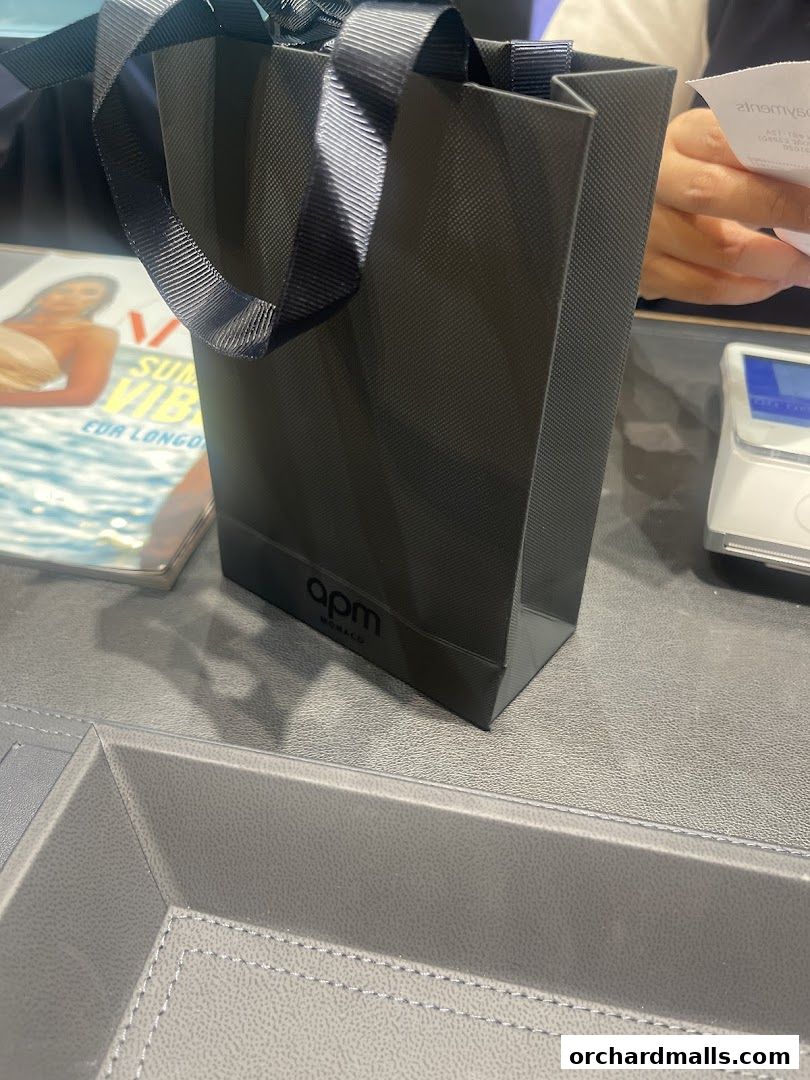 A black APM Monaco shopping bag sits on a counter next to a receipt and a scale.
