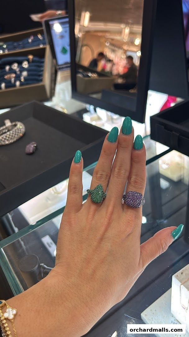 A hand with teal nail polish wearing two sparkling rings, one green and one purple.