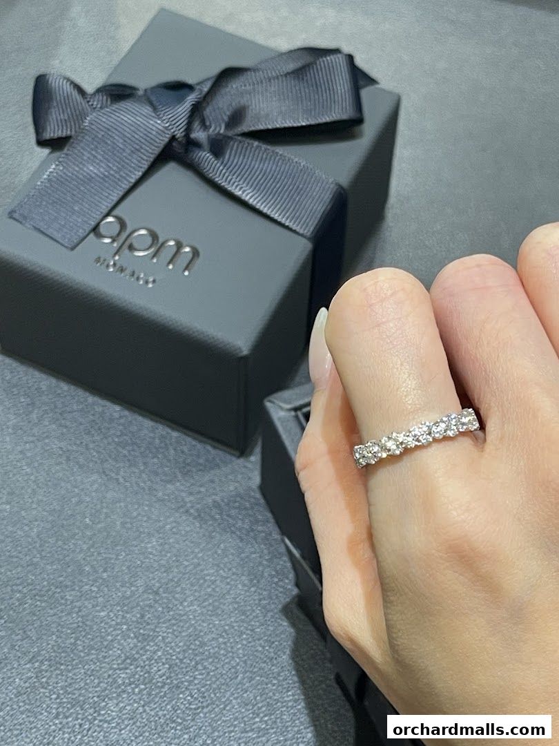 A hand wearing a diamond ring next to an APM Monaco gift box.