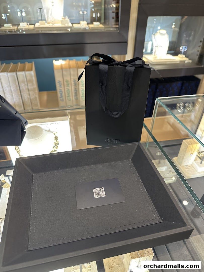 A black gift bag with a ribbon and a card on a tray inside a jewelry store.