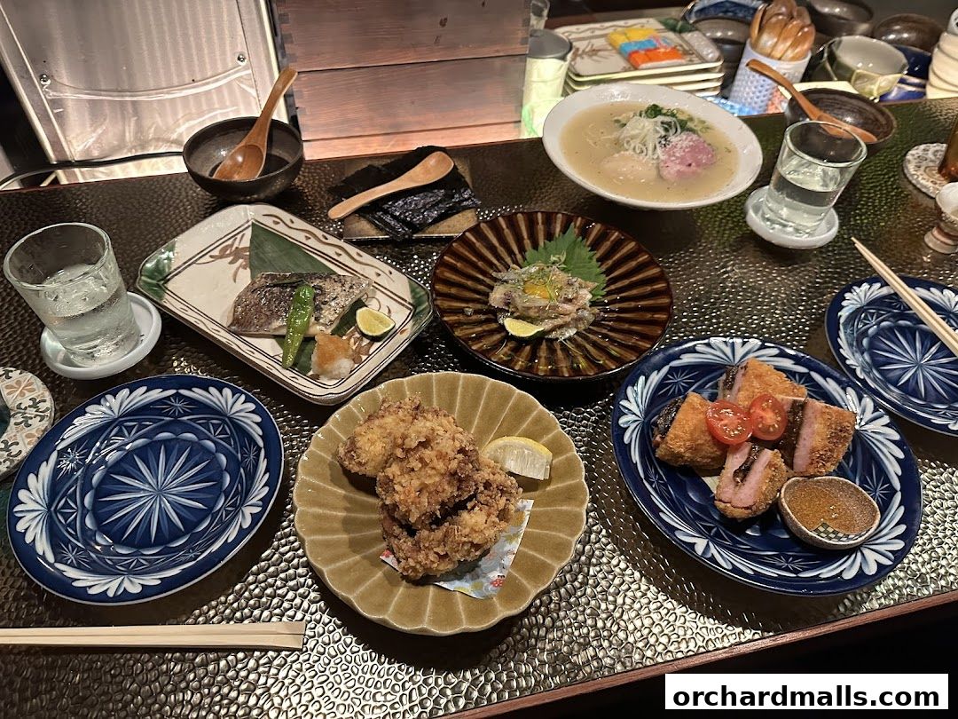 A table laden with various Japanese dishes, including fried chicken, grilled fish, and ramen.