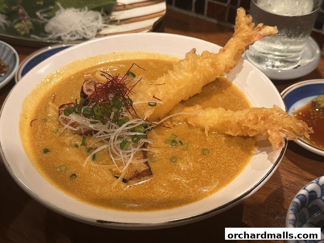 A bowl of creamy curry soup with tempura shrimp and garnishes.