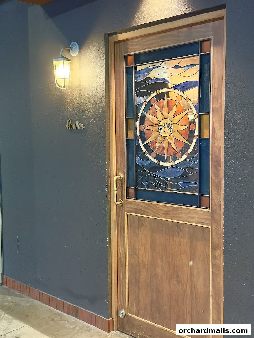 The entrance to Apollon features a wooden door with a stained-glass sun motif and a brass handle.