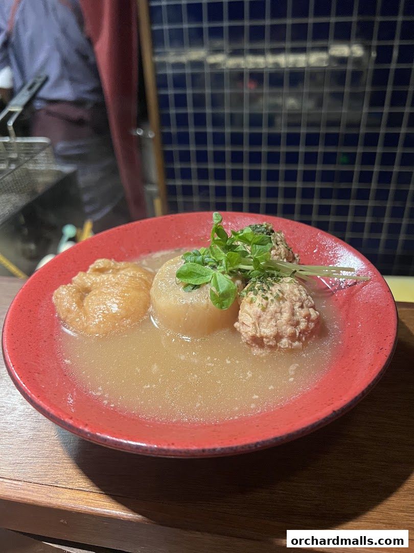 A close-up of a red bowl filled with oden, a Japanese stew, with daikon radish and meatballs.