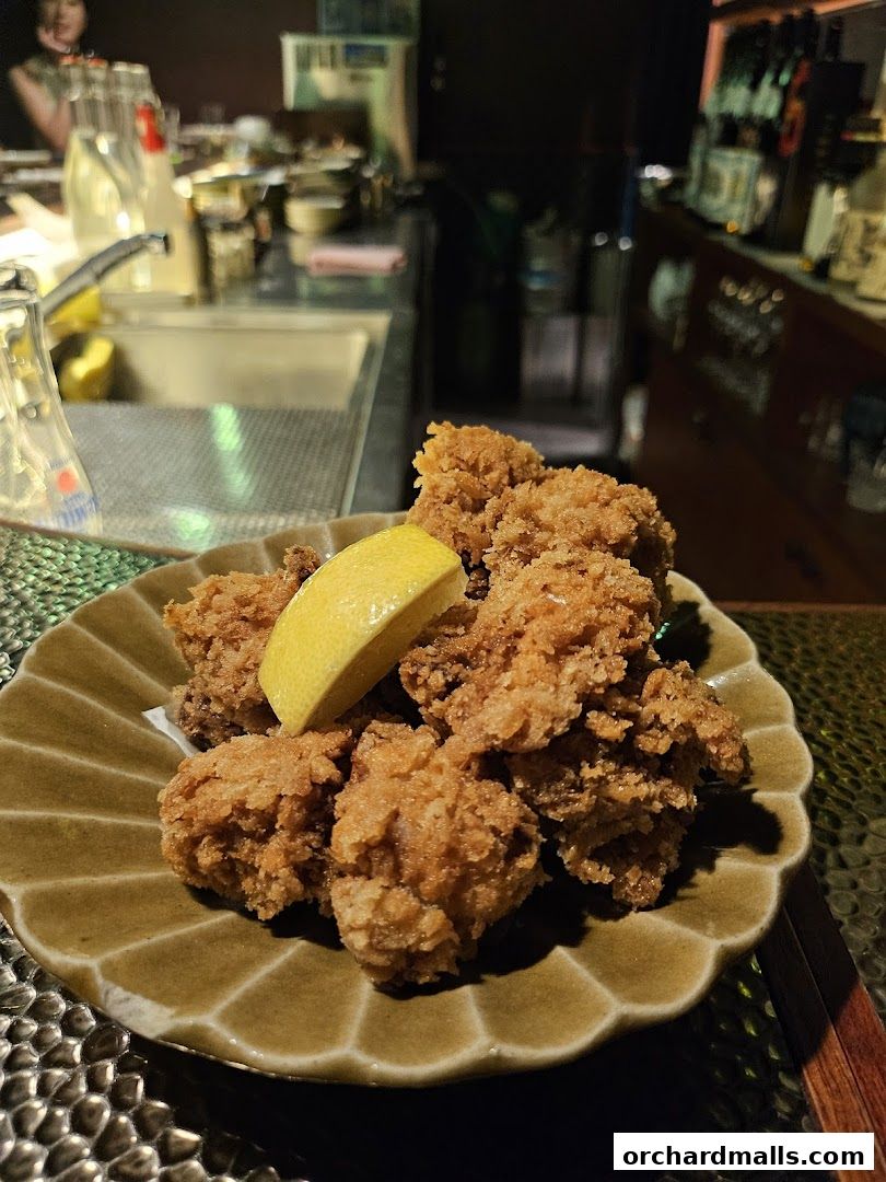 A plate of crispy fried chicken with a lemon wedge, served in a dimly lit restaurant.