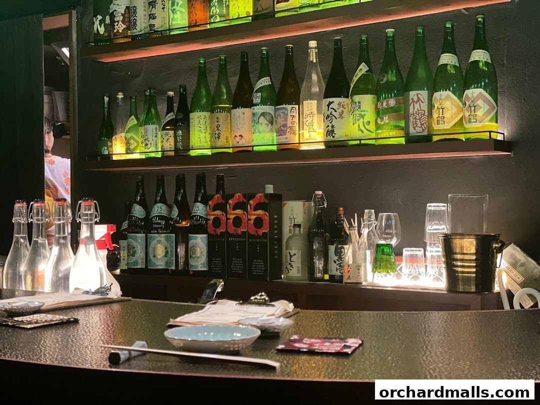 A bar counter with shelves of sake bottles and various glassware.